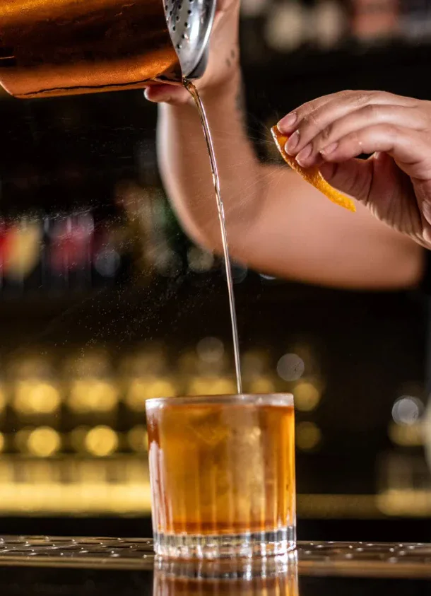Bartender servindo coquetel em copo baixo com casca de laranja